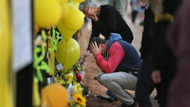 GRIEVING: Merrilyn Scott, the mother of Stephanie Scott, and Aaron Leeson-Woolley, Stephanie's fiance, at the floral memorial on the gates of the high school where she worked.