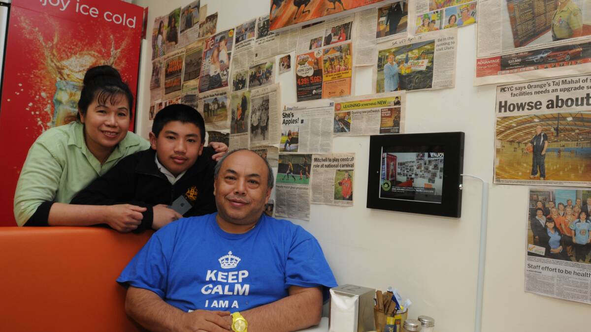 SHOWING THE NEWS: Cheeky Barista owner Sopee Soo, son Sebastian and fellow cafe owner Rodney Soo against the wall of newspaper clippings collected and hung in the cafe this year. Photo: JUDE KEOGH 	 0624cheekybarista2 