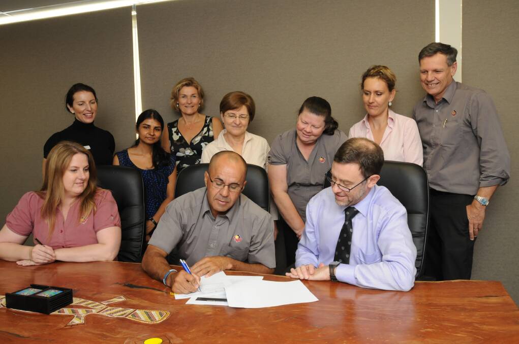 PEN TO PAPER: Orange Aboriginal Medical Service CEO Jamie Newman and Mark Arnold of The University of Sydney sign the agreement contract watched by Yolande Meintjes (seated), Amanda Croft, Latika Naidu, Catherine Hawke, Judy Ross, Ann-Marie Kable, Annemarie Woltmann and Rick Aitken. Photo: STEVE GOSCH                                                                               0313sgoams4
