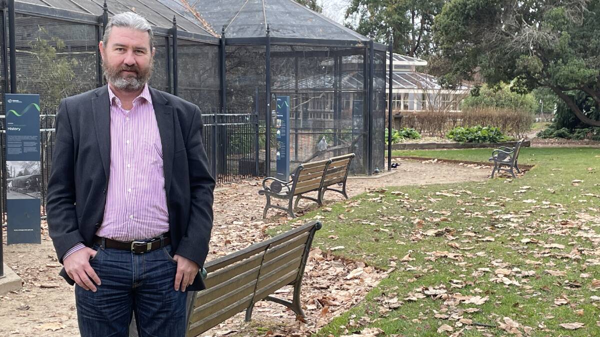 Cr David Mallard in front of Cook Park's bird aviary, with the historic Blowes Conservatory in the background. The report suggests the aviary could be removed or relocated. 