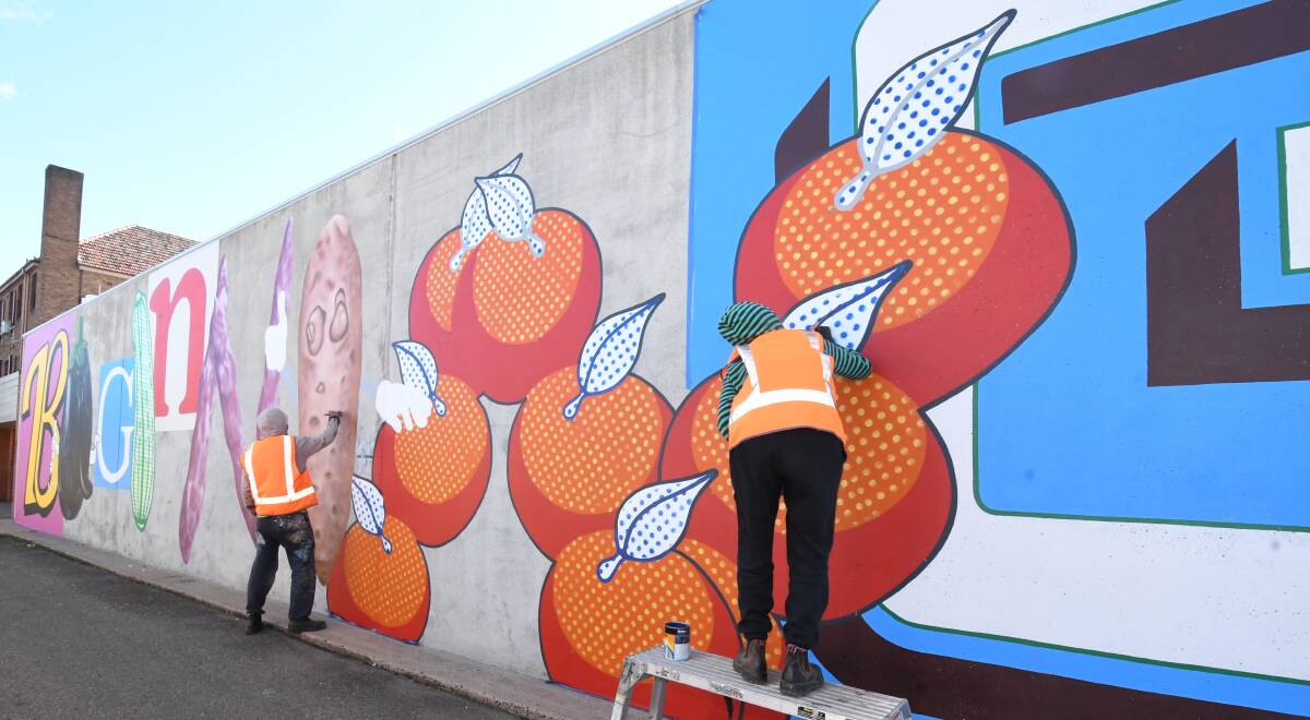 TEAM: Tully and Bianca Moore turn a big grey wall into a fruity piece of street art off McNamara Street. Photo: JUDE KEOGH
