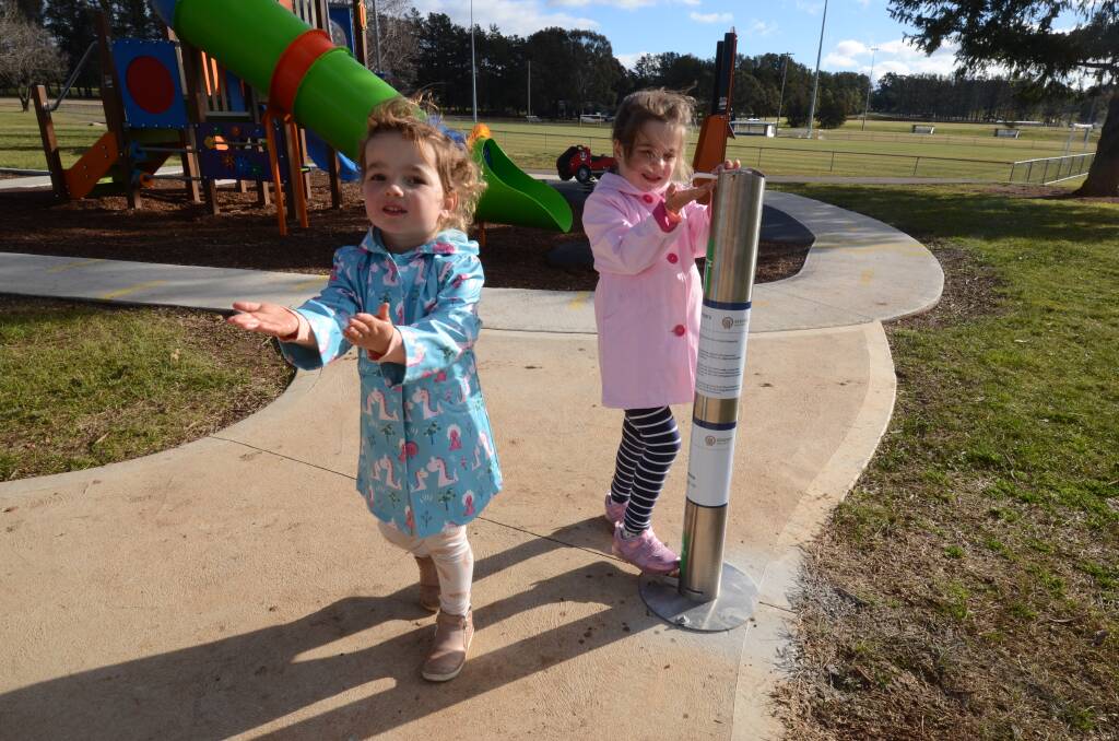 CLEAN START: Maddy and Zoe Murray use a new hand-sanitiser bollard at the playground in Sir Jack Brabham Park. Photo: JUDE KEOGH