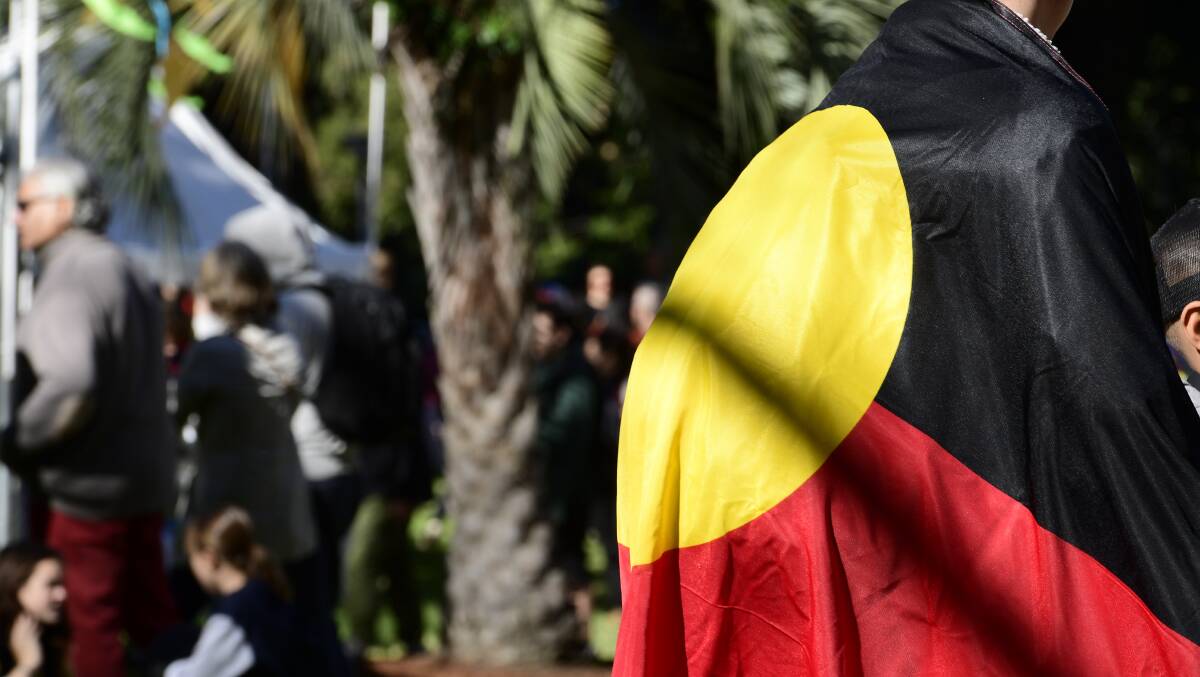 REMEMBER: A member of the public is seen with the Aboriginal flag during the City of Sydney's annual NAIDOC in the City event in Hyde Park. Photo: AAP/Bianca De Marchi