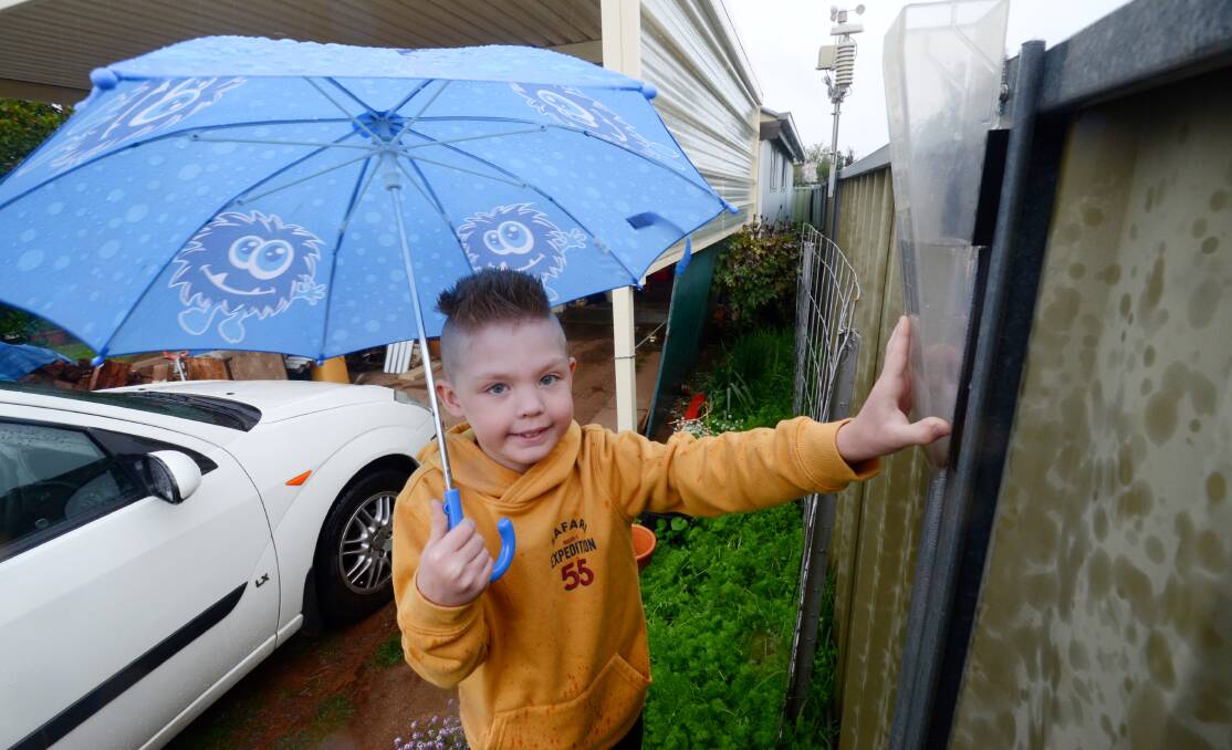 HIGH RAINFALL: Aiden Ford protects himself from the rain on Friday while he checks the family's rain gauge to see how much rain had fallen on Friday. Photo: JUDE KEOGH
