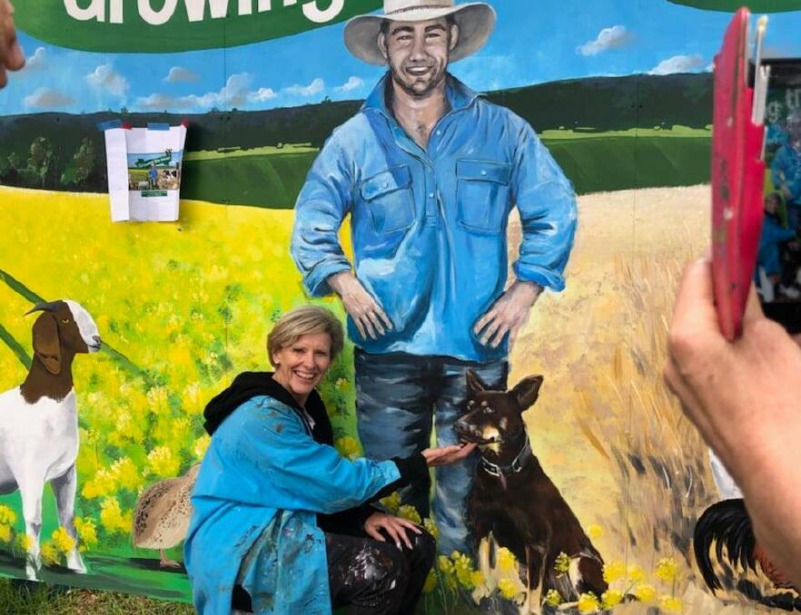 VIVID: Artist Cheryl McLean posing in front of a mural in Eugowra created for the National Farmers Federation. Photo: SUPPLIED.