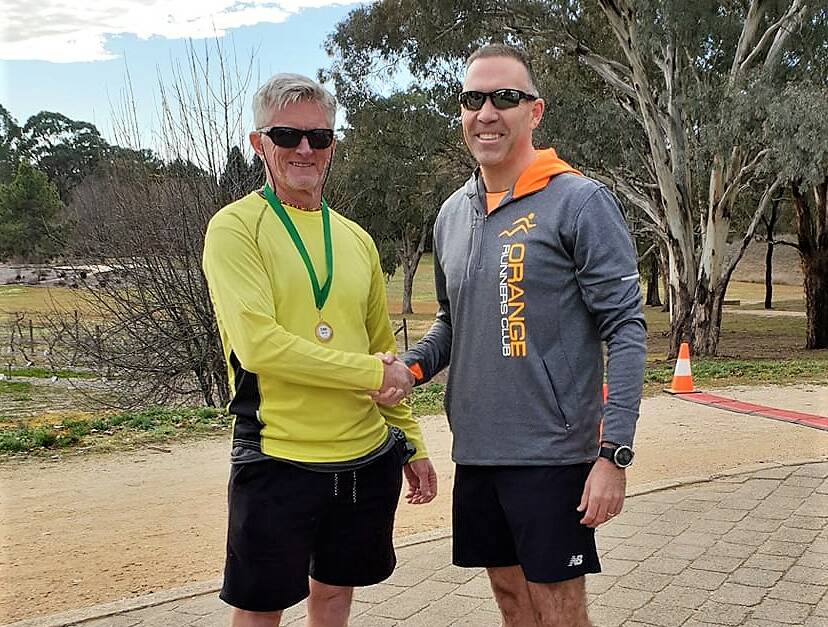 MILESTONE: 'Magic' Mike Cooper receiving his 700 club run recognition medal from Oranges Runners Club president Anthony Daintith at Sunday's Botanic Gardens club run. Photo: CONTRIBUTED