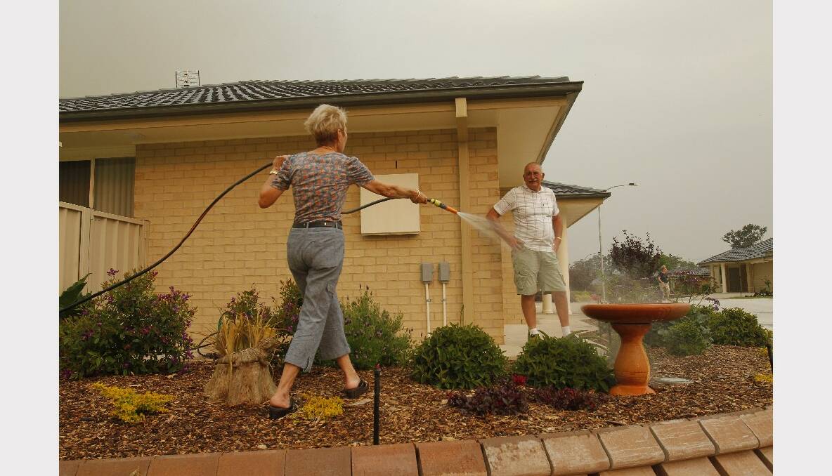 Bushfire in forest near Lake Road, Elermore Vale. Residents of Elermore Glen housing estate, Robin Collin and Barry Collin watering their garden after the woodchips started catching fire. Photo: Max Mason-Hubers, Newcastle Herald.